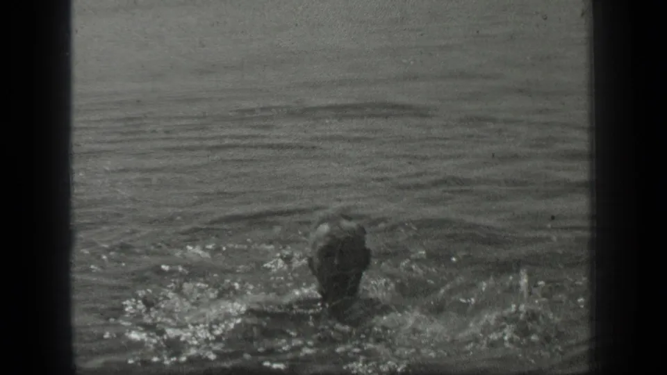 A swimmer in a cap moves through Long Lake, Canada, in 1939 home-movie footage, with ripples and splashes surrounding the head and shoulders.