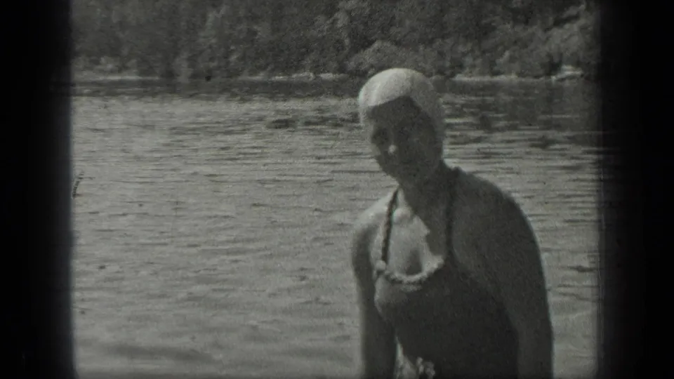A woman in a swim cap and vintage swimsuit stands near Long Lake, Canada, turned toward the camera in a soft 1939 8mm frame.