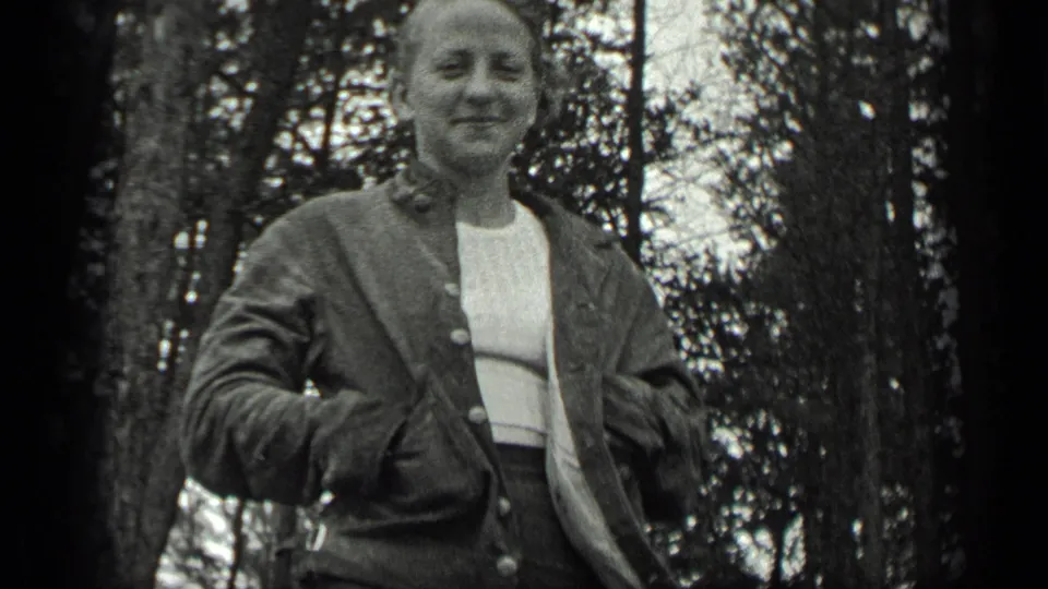 In 1939 Long Lake, Canada home-movie footage, a woman smiles toward the camera among tall trees while wearing a button-up jacket.
