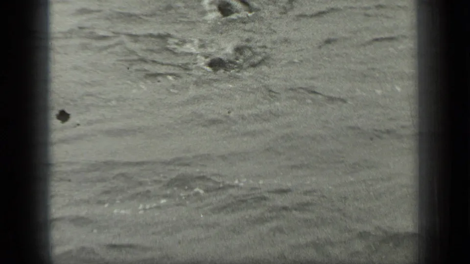 A swimmer is partly visible in rippled water in the Long Lake, Canada home-movie sequence, framed by dark 8mm film edges.
