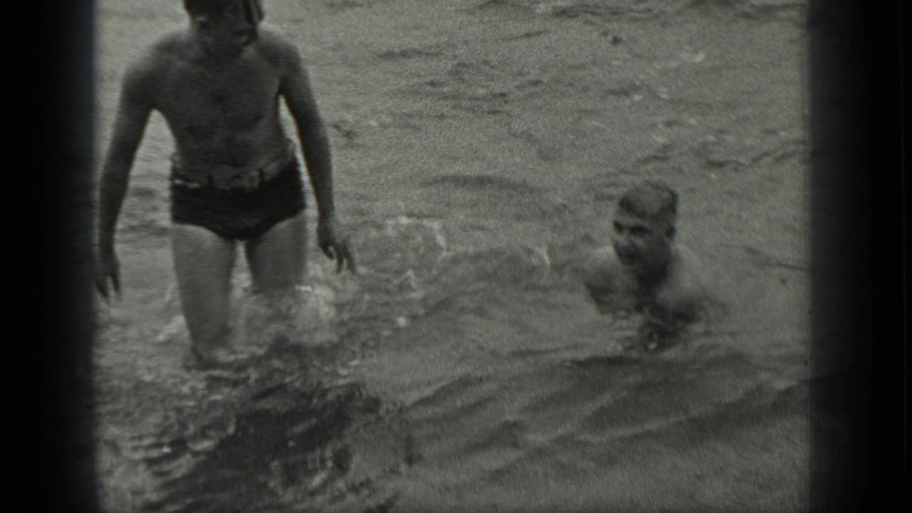 One man stands in shallow water while another swimmer is nearby.