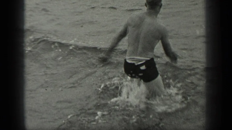 The swimmer is seen from behind in dark trunks as he turns away in shallow water in the 1939 Long Lake home movie.