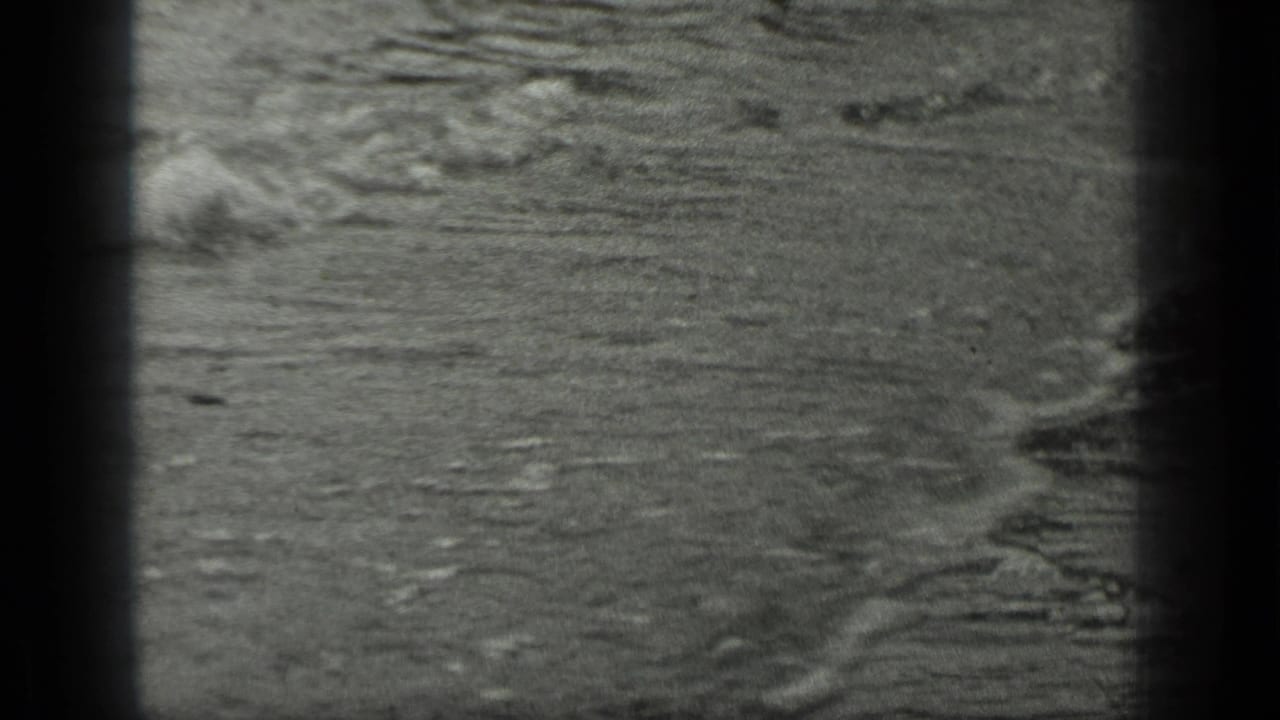 Dark-framed 8mm view of rippled water and small waves near shore.