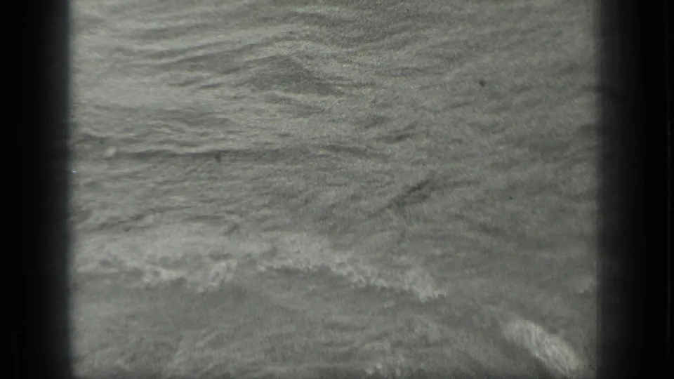 1939 Long Lake, Canada frame showing a low wave line and foam moving across a sandy shoreline.