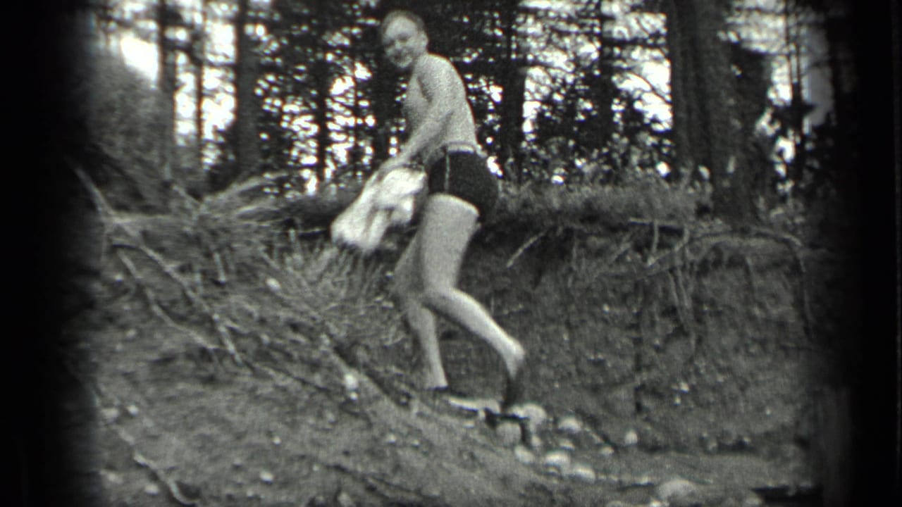 Man with towel steps down a wooded dirt bank toward the water.