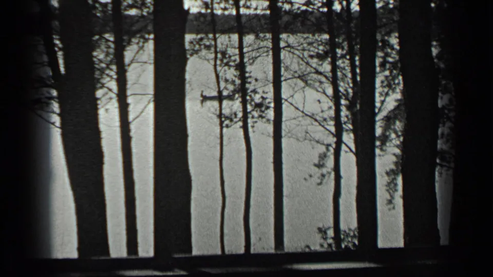 1939 Long Lake, Canada home-movie frame showing dark foreground trees, still water, and a small rowboat in the distance.