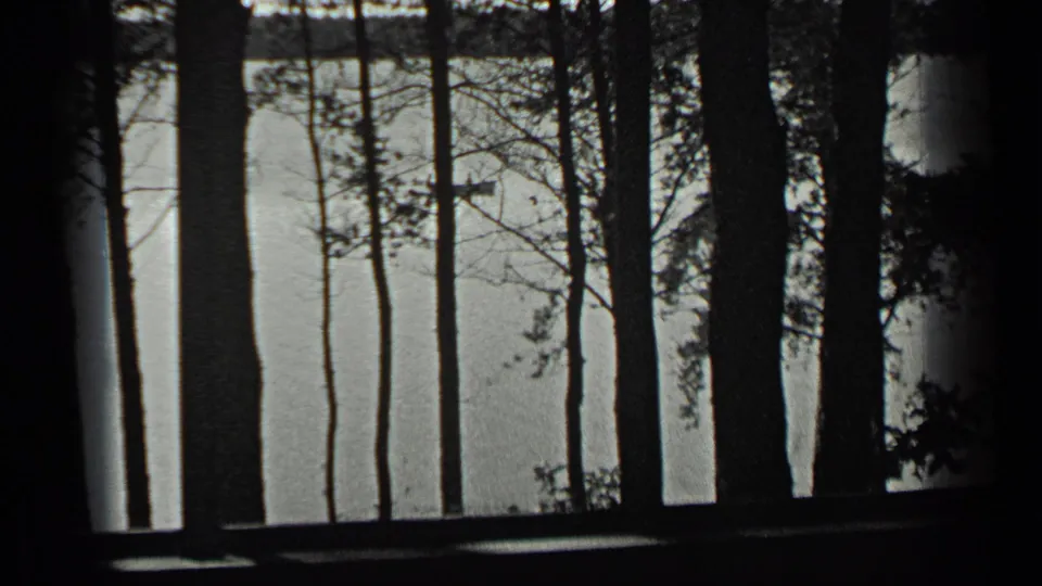 Final 1939 Long Lake frame with dark lakeside trees in the foreground and calm water stretching toward the far shore.