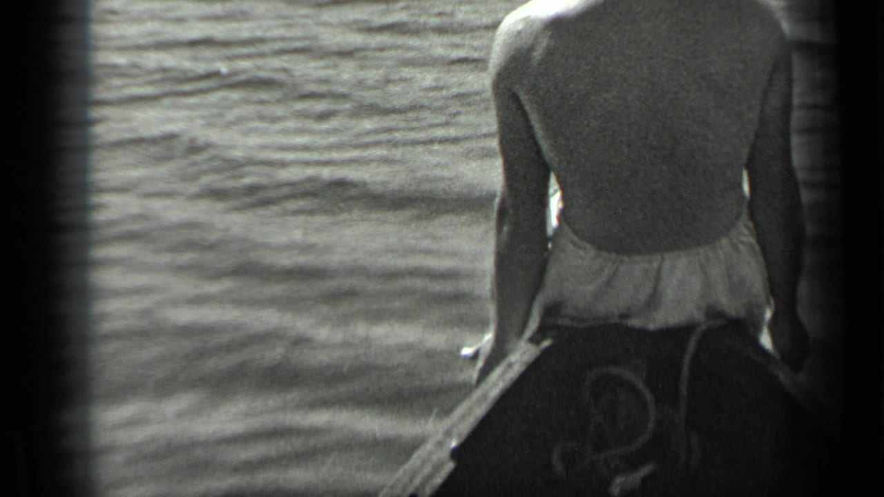 Man in a swimsuit seated at the bow of a small boat on open water.