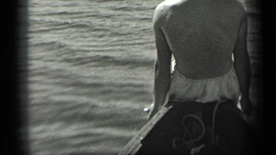 A man in a swimsuit sits facing forward at the bow of a small boat on Long Lake, Canada in 1939.