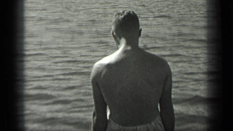 Back view of a seated man in a swimsuit riding at the bow of a small boat on Long Lake, Canada in 1939.