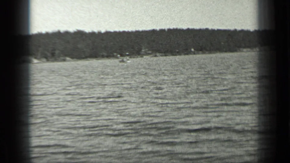 Long Lake, Canada, shown as rippled water with a dark tree-lined shore and small distant structures in 1939 home-movie footage.