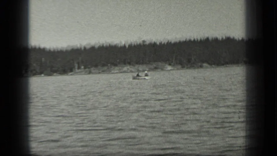 A small boat carrying visible people moves across Long Lake, Canada, with wooded shore behind it in 1939 8mm footage.