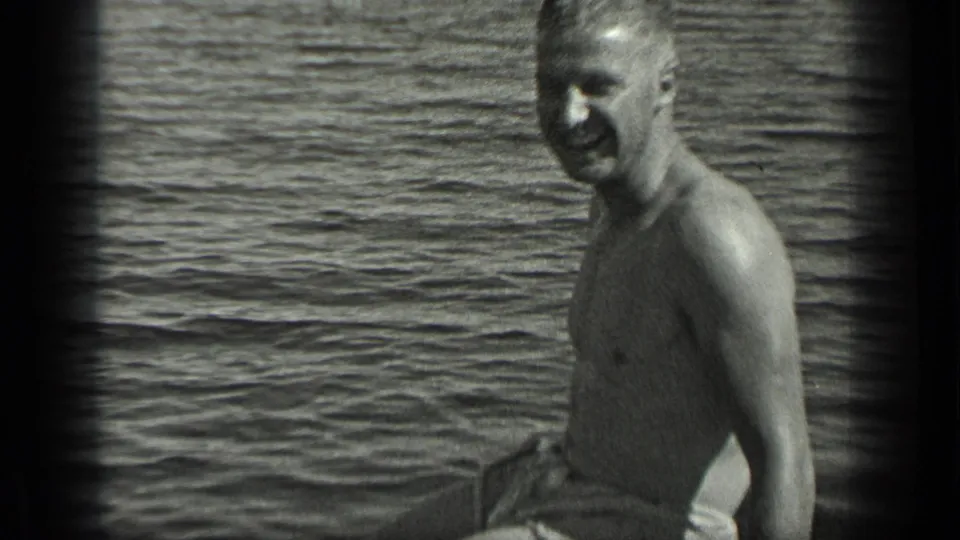 A man smiles toward the camera while seated in a small boat on Long Lake, Canada, in 1939 home-movie footage.