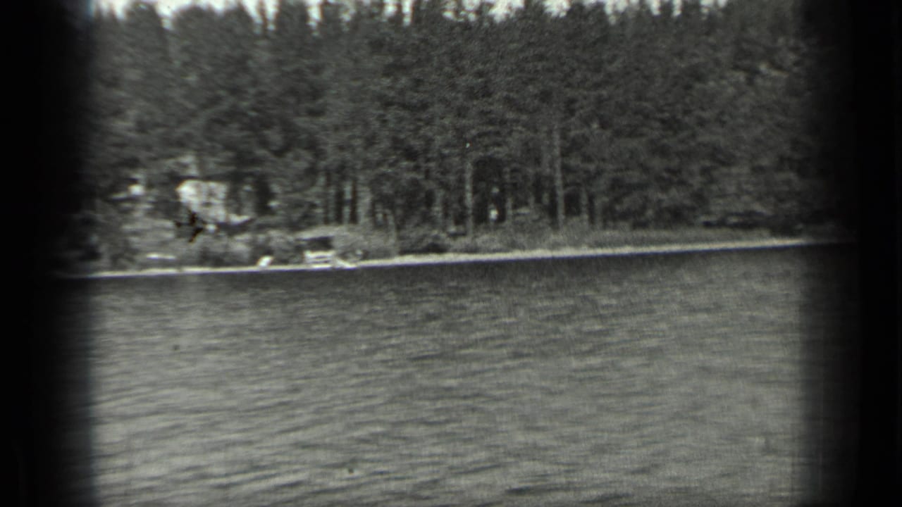 Rippling lake water with a wooded shoreline and small pale structure at left.