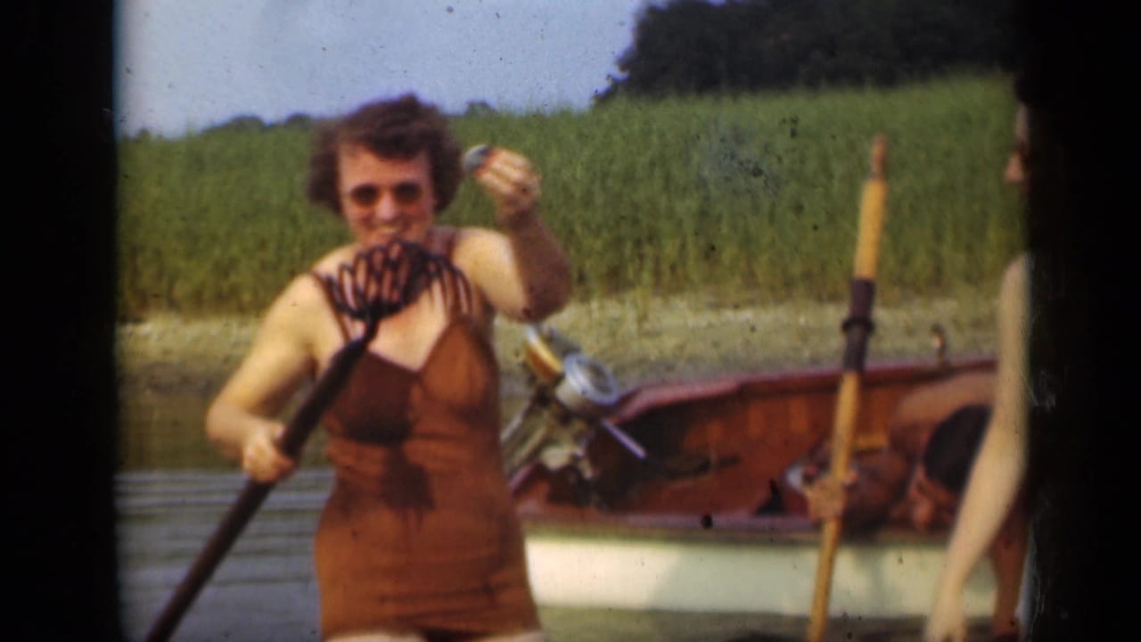Woman in a brown swimsuit holds a rake-like tool while standing near a rowboat.
