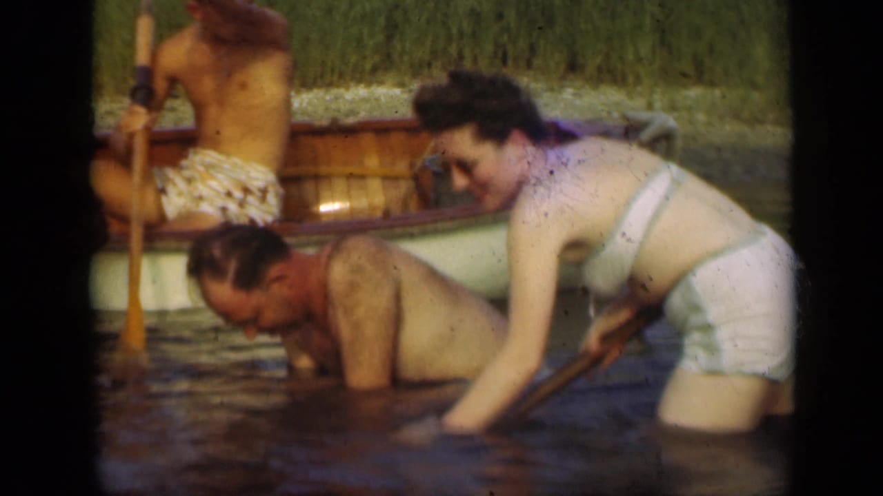 1948 Long Island home-movie frame of adults wading beside a small rowboat in shallow lake water.