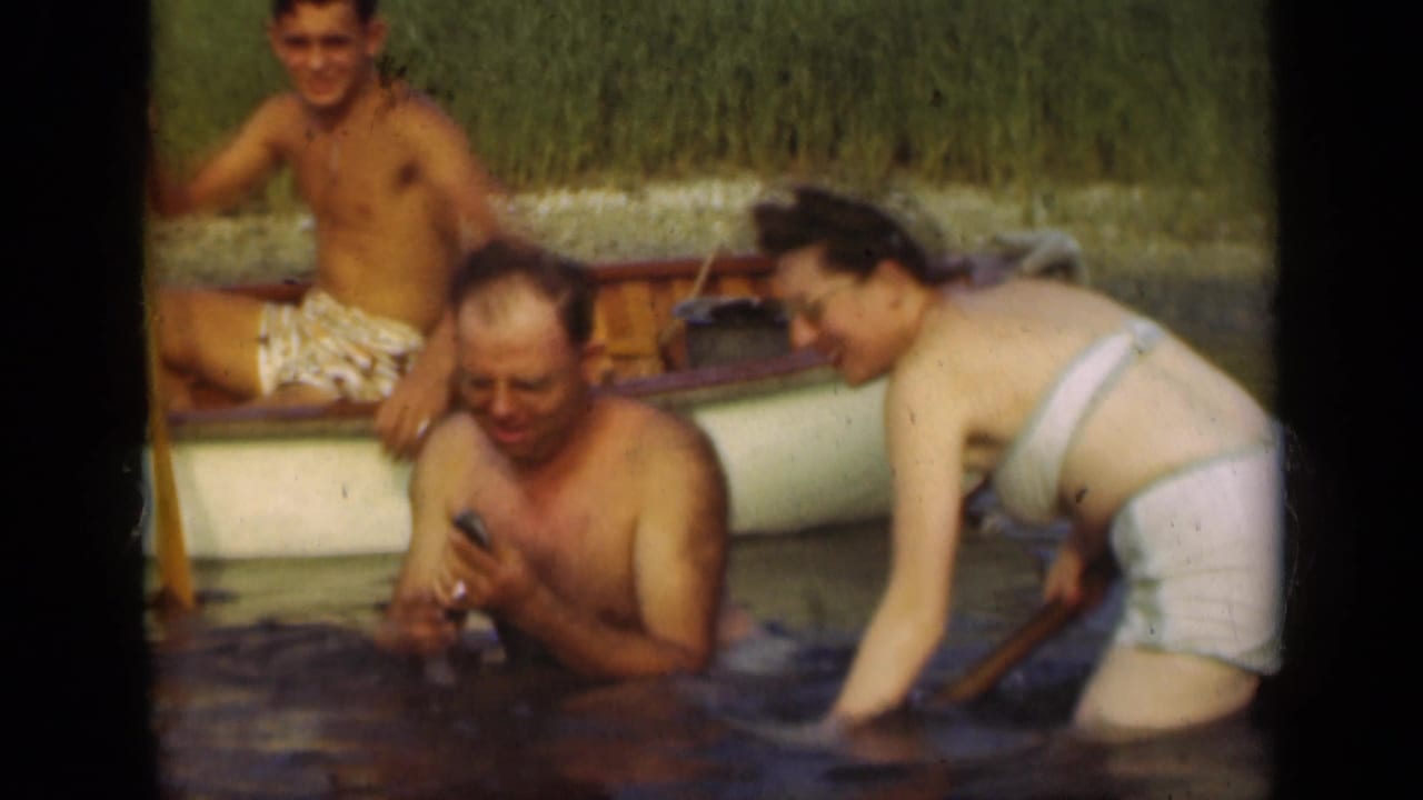 1948 Long Island lake frame with two adults wading near a small rowboat and another adult seated inside.