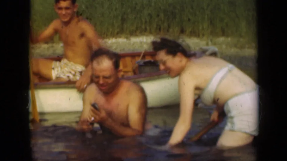 1948 Long Island lake frame with two adults wading near a small rowboat and another adult seated inside.