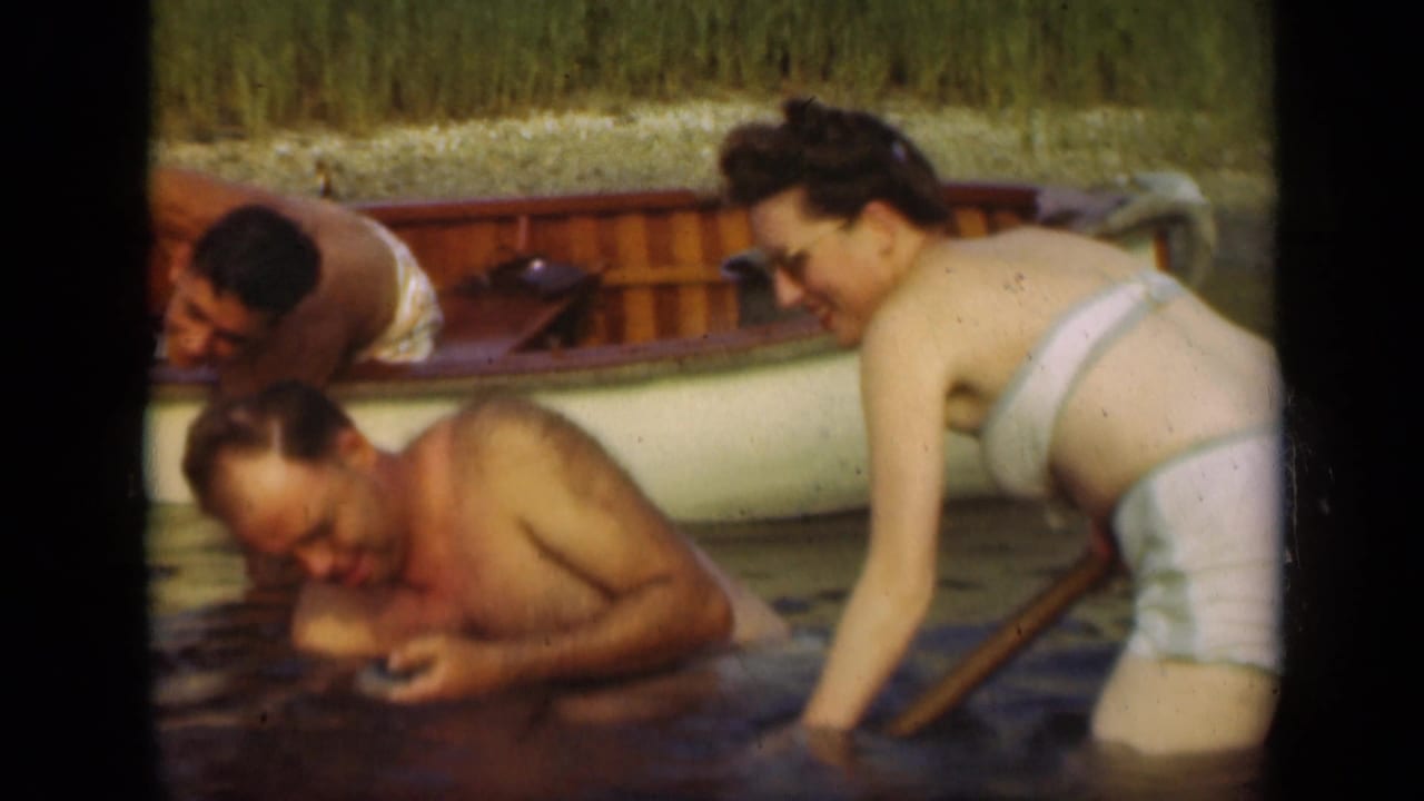 1948 Long Island lake frame showing adults laughing and wading beside a small rowboat in a home-movie scene.