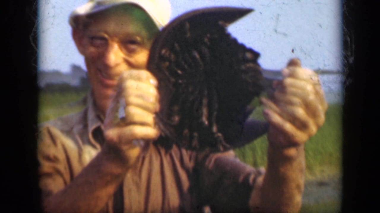 Man in cap holds a horseshoe crab toward the camera outdoors.
