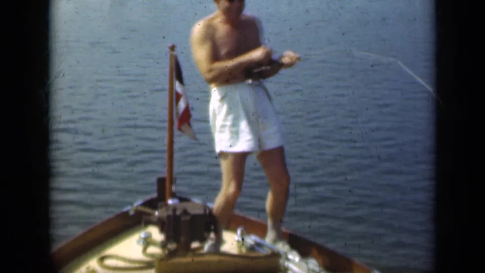 The closing frame shows the man beside the small flag on the bow, holding a bent fishing rod against a wide background of calm water.