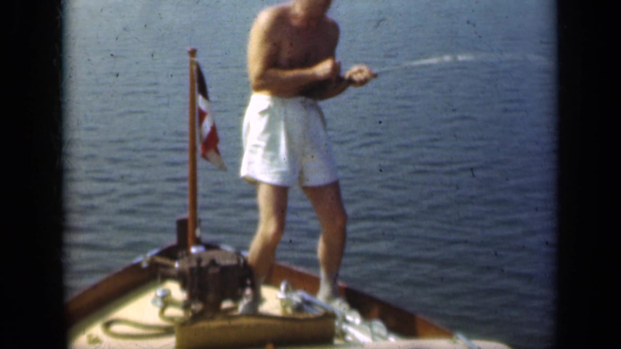 In 1948 Long Island footage, a shirtless man in white trunks stands at the bow of a small boat with a fishing rod and flagstaff nearby.