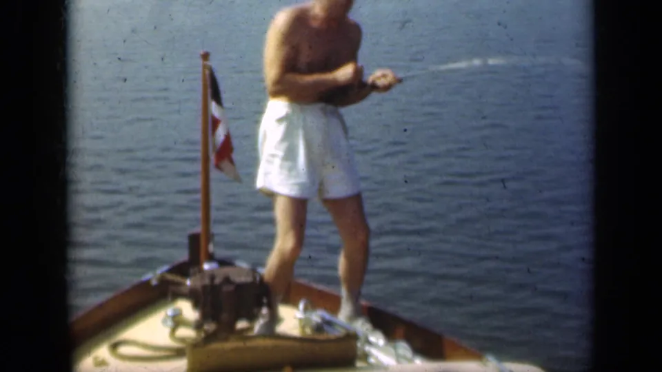 In 1948 Long Island footage, a shirtless man in white trunks stands at the bow of a small boat with a fishing rod and flagstaff nearby.