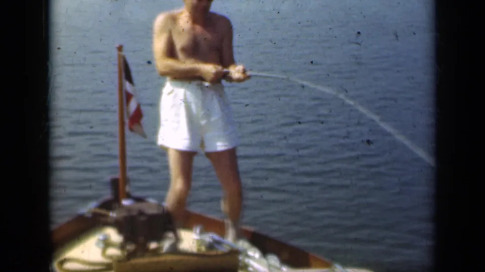 The man keeps the rod angled as a fishing line curves across the water beside the small boat in the 1948 Long Island home movie.