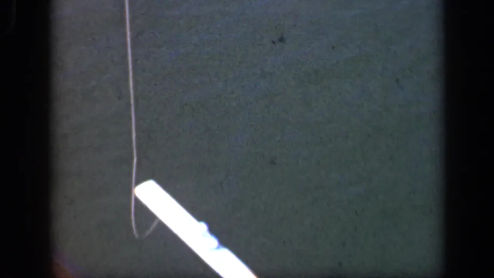 Home-movie close-up of a fishing line near a pale boat-edge or rod detail over dark green water in Long Island footage.