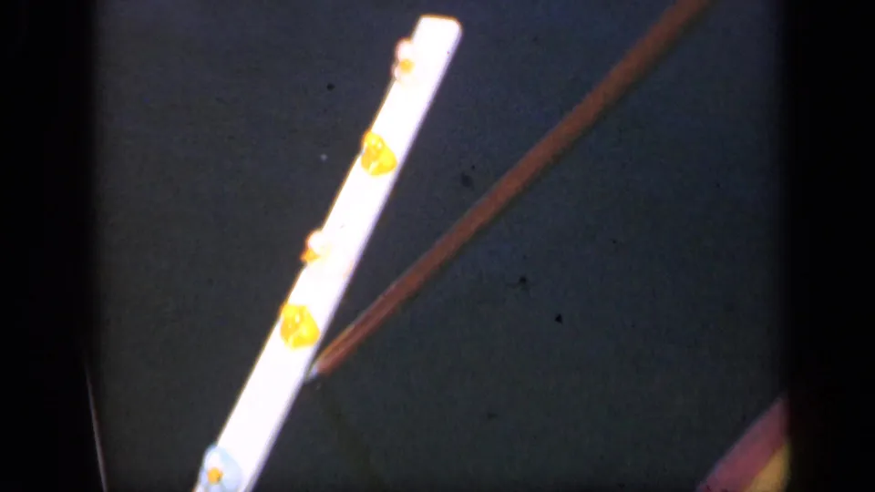 1948 Long Island 8mm frame showing a diagonal pointer beside yellow gum-like spots on a bright strip.