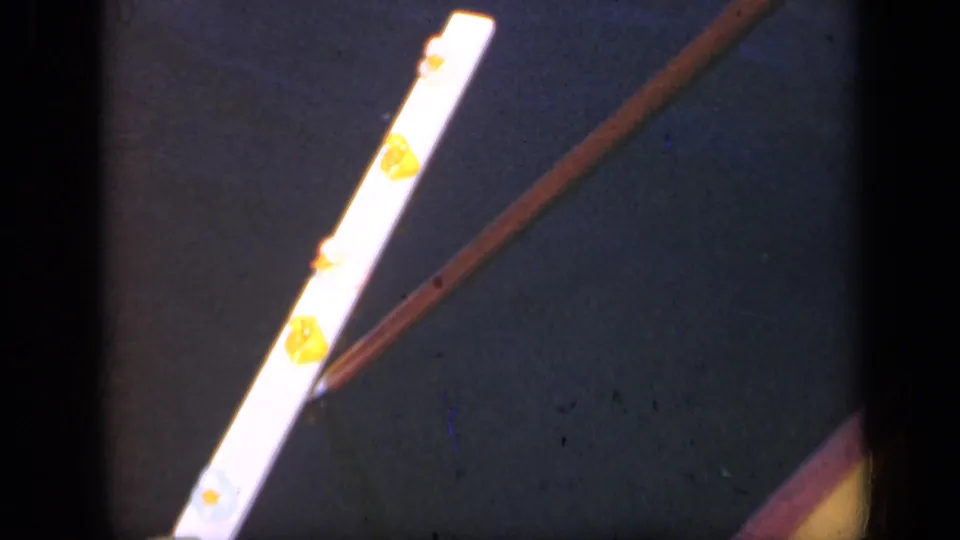 Close 1948 Long Island home-movie view of the white and yellow object with a brown rod crossing near it in bright light.