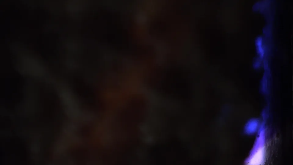 Dark transitional 8mm frame with indistinct forms and blue-purple light at the right edge in the Long Island home movie.