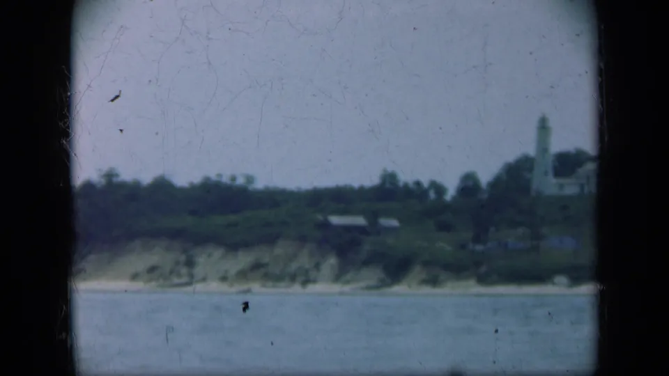 Distant 1948 Long Island coastal view with a lighthouse, trees, shoreline bluff, and calm water in the foreground.