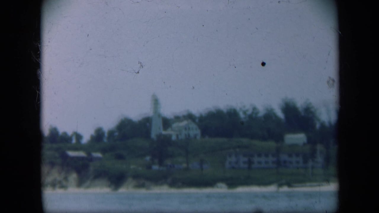 Distant white lighthouse and coastal buildings above a shoreline, framed by 8mm film borders.