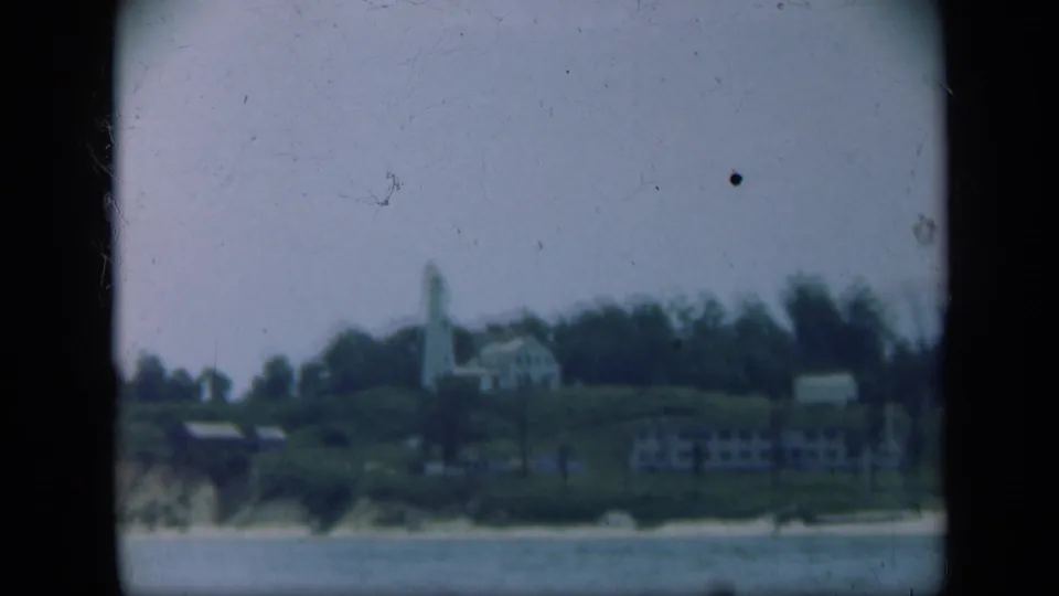 1948 Long Island 8mm frame showing a white lighthouse and nearby buildings on a grassy bluff above the sea.
