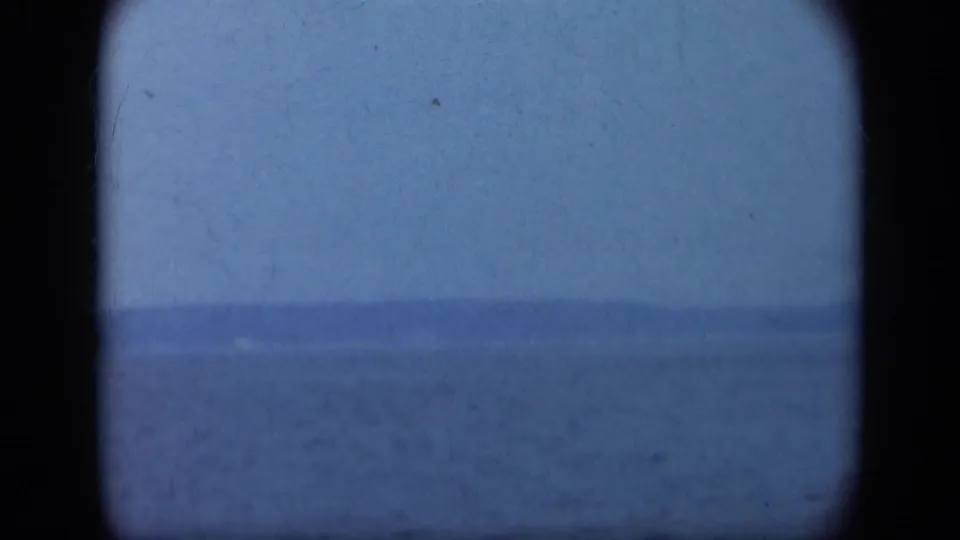 Faded 8mm Long Island coastal frame showing calm sea, distant land, and overcast blue-gray sky.