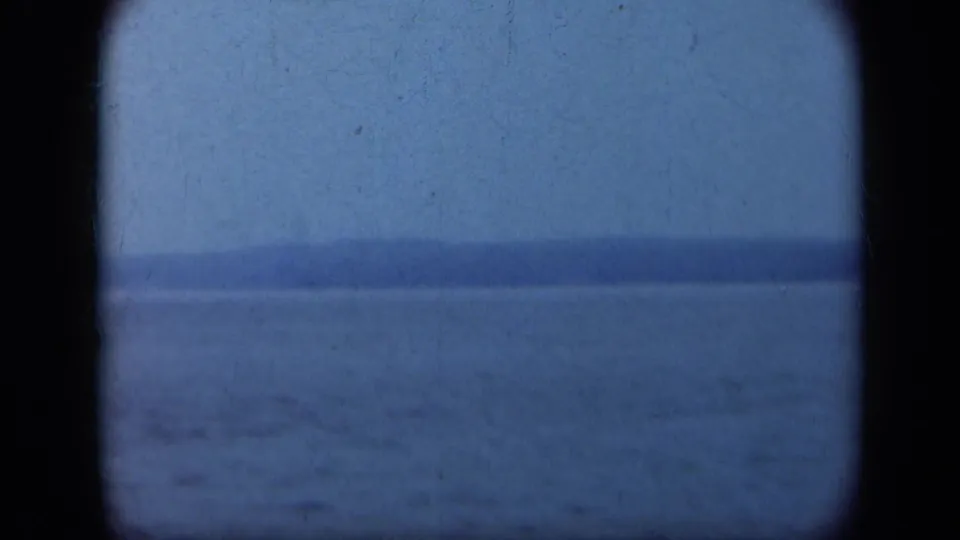 1948 Long Island home-movie frame of blue-toned water and a far shoreline, softened by grain, exposure, and rounded 8mm borders.