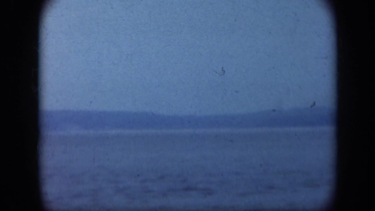 Blue-tinted water and hazy horizon seen through dark rounded film-frame edges.