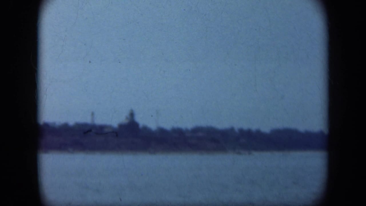 Distant shoreline seen across water through a dark rounded 8mm frame.