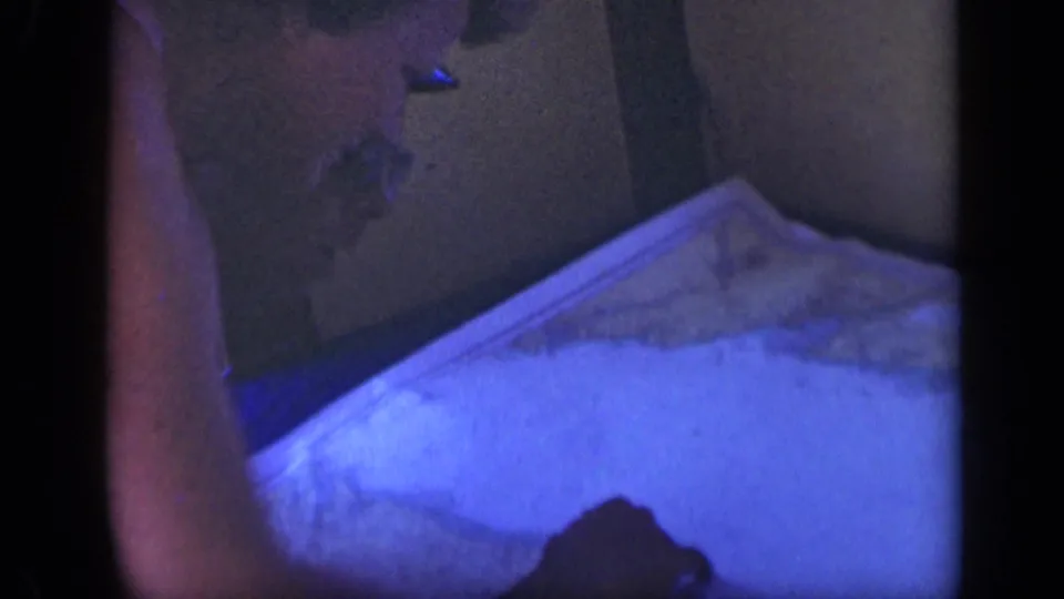 Two adults appear close together over a large chart in a dark, blue-tinted ship cabin in the Long Island 1948 home movie.