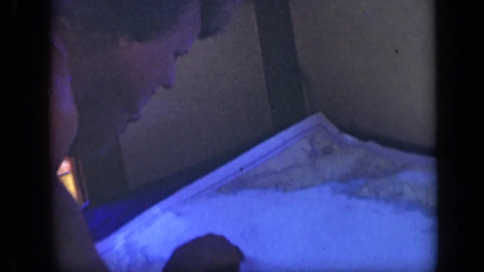 A man in a dim shipboard cabin looks down toward a large chart, with dark panels and blue 8mm exposure visible.
