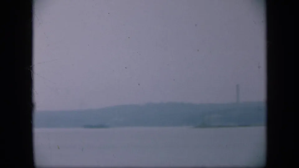 1948 Long Island shoreline view with calm water, muted sky, distant land, and dark frame borders from the scanned home movie.