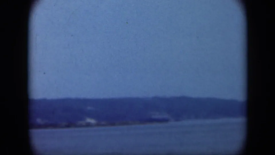 Blue-gray 8mm frame of Long Island water and low shoreline, with soft focus, dark border edges, and visible film texture.