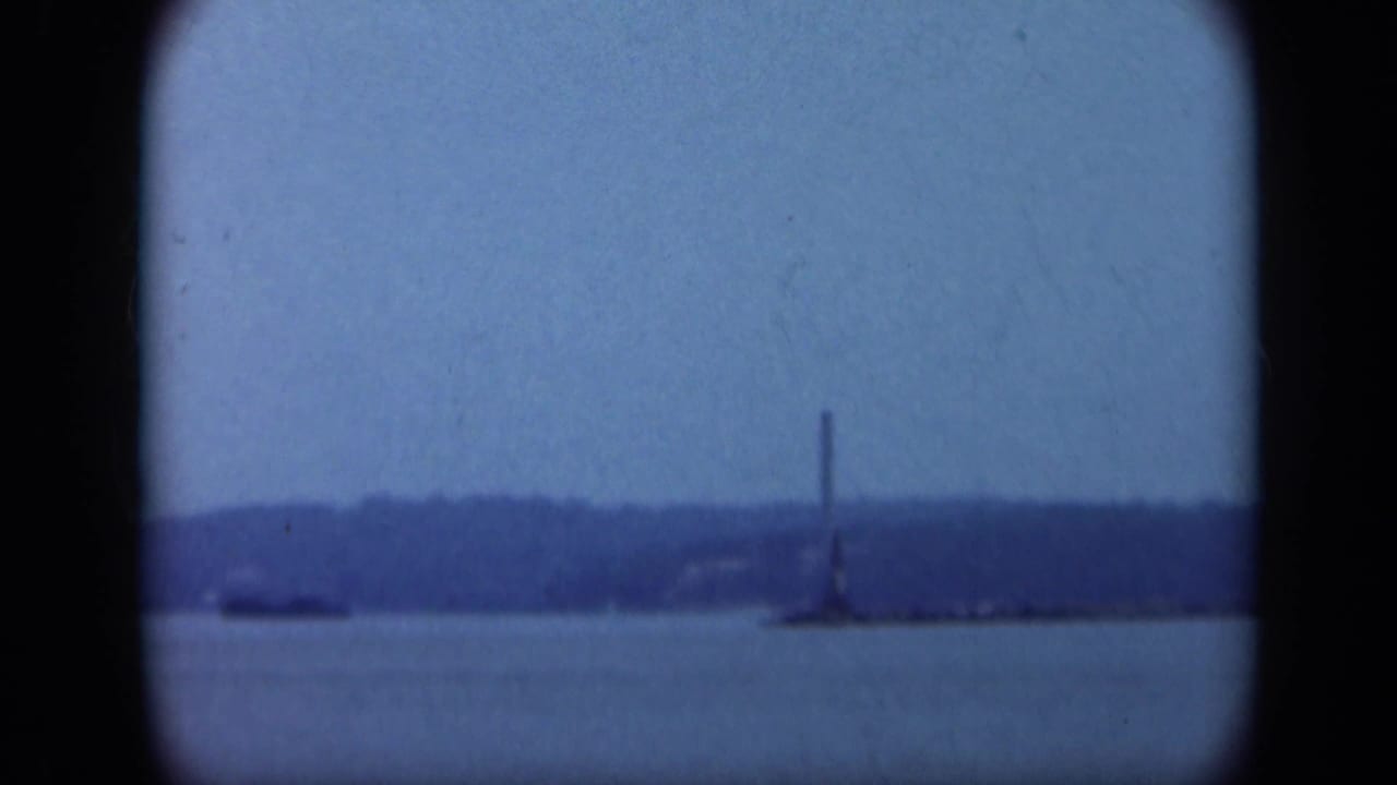 Distant lighthouse or tower across calm water beneath a blue sky.