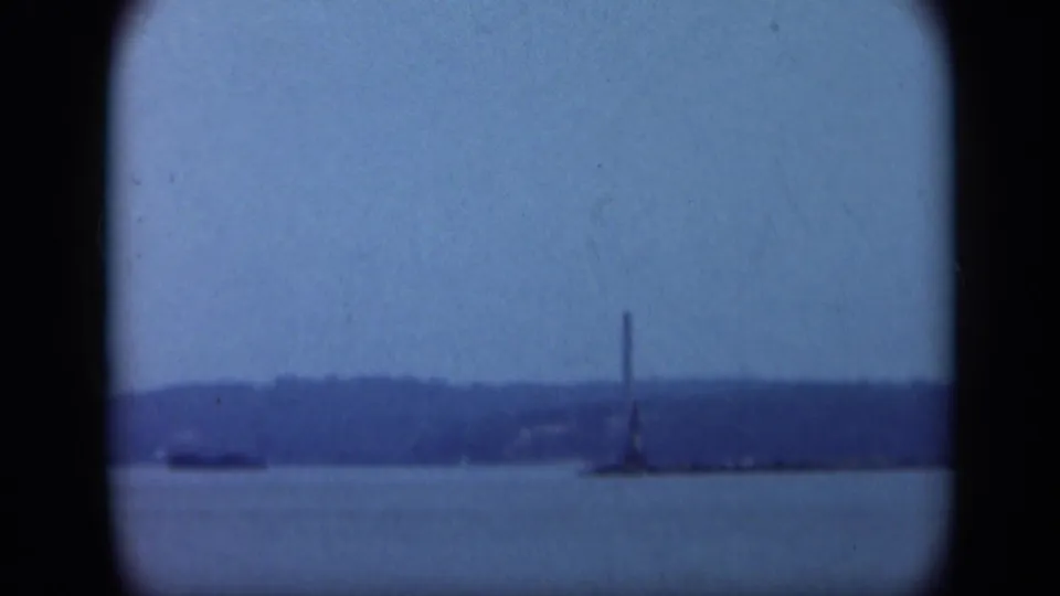 1948 Long Island 8mm frame showing calm water, low shoreline, and a distant lighthouse or tower shape in soft blue light.