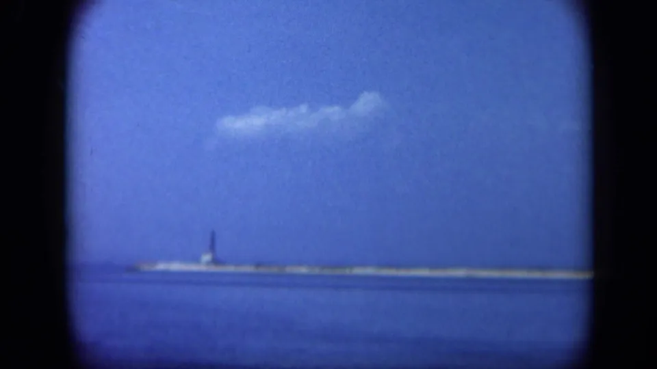 Distant Statue of Liberty viewed from Long Island across open water, framed by the rounded edge of 8mm film.