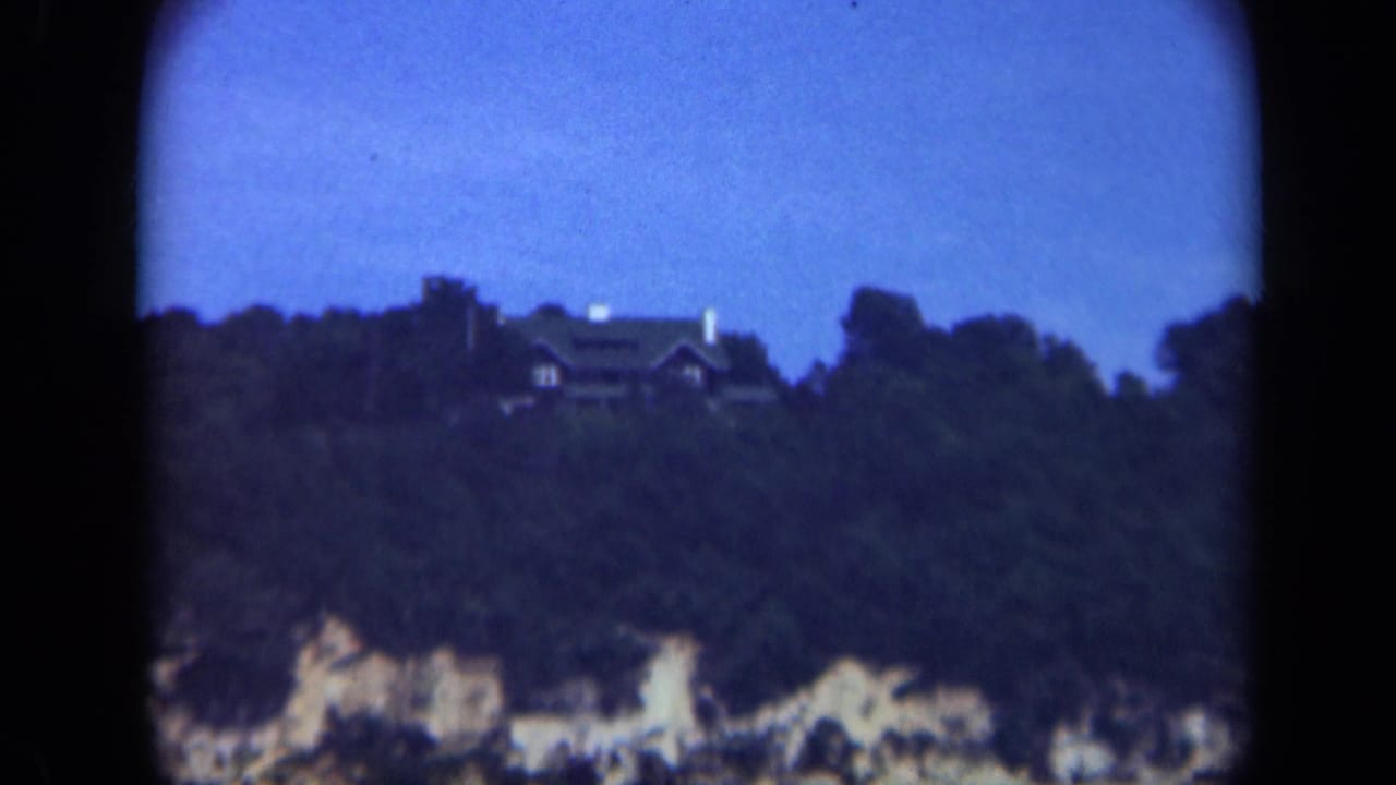 Distant houses sit above a wooded hillside and pale bluff under a blue sky.