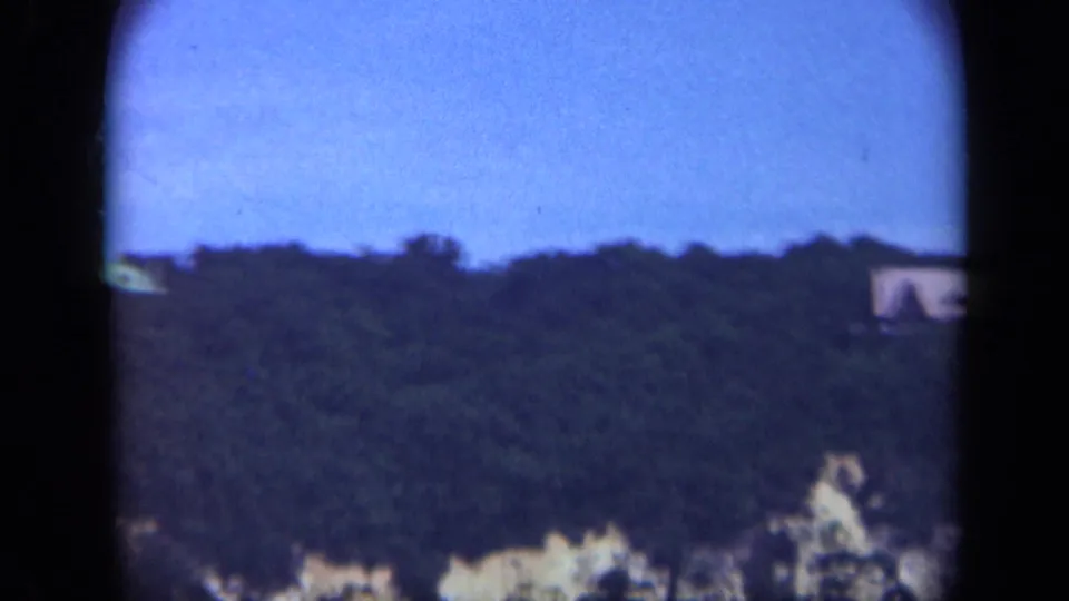 1948 Long Island home-movie frame showing a wooded ridge, pale bluff, and partial distant buildings near the frame edges.
