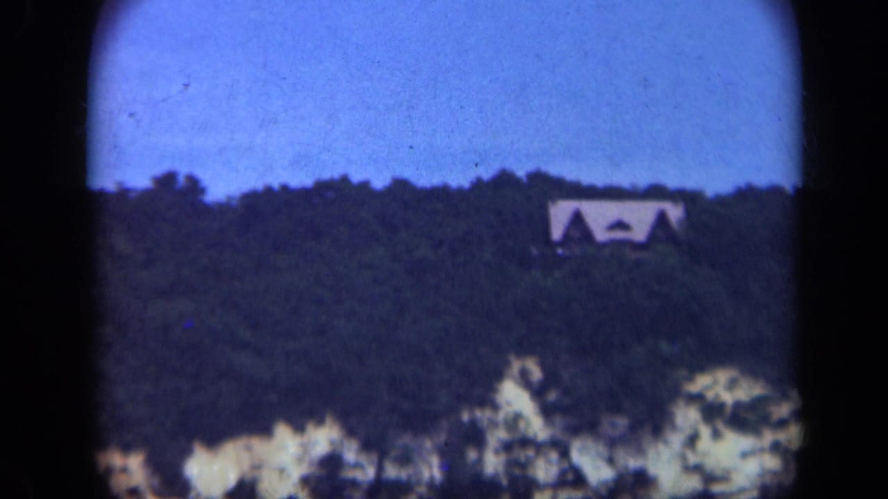 Distant light-colored house above a dark wooded hillside under a blue evening sky.