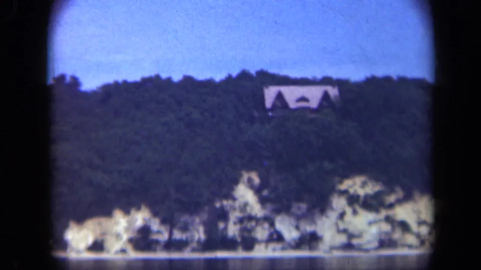 1948 Long Island home-movie frame with a distant residence on a dark tree-covered hill overlooking water.
